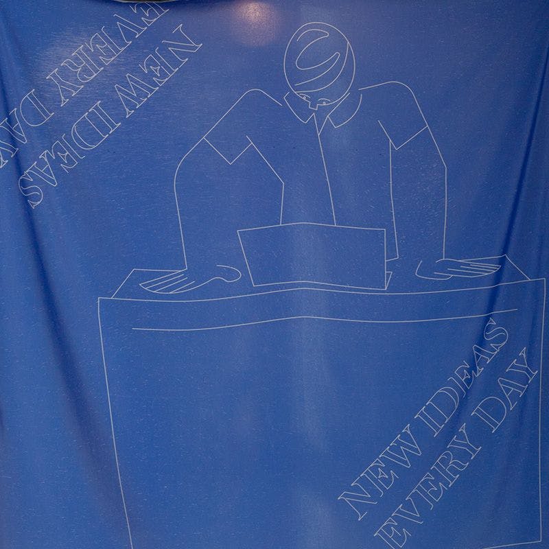 A blue silk flag displaying a drawing a person standing in front of a laptop